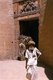 India: A heavily laden camel enters Surya Pol (Surya Gate) as a Rajasthani man exits, Jaiselmer, Rajasthan